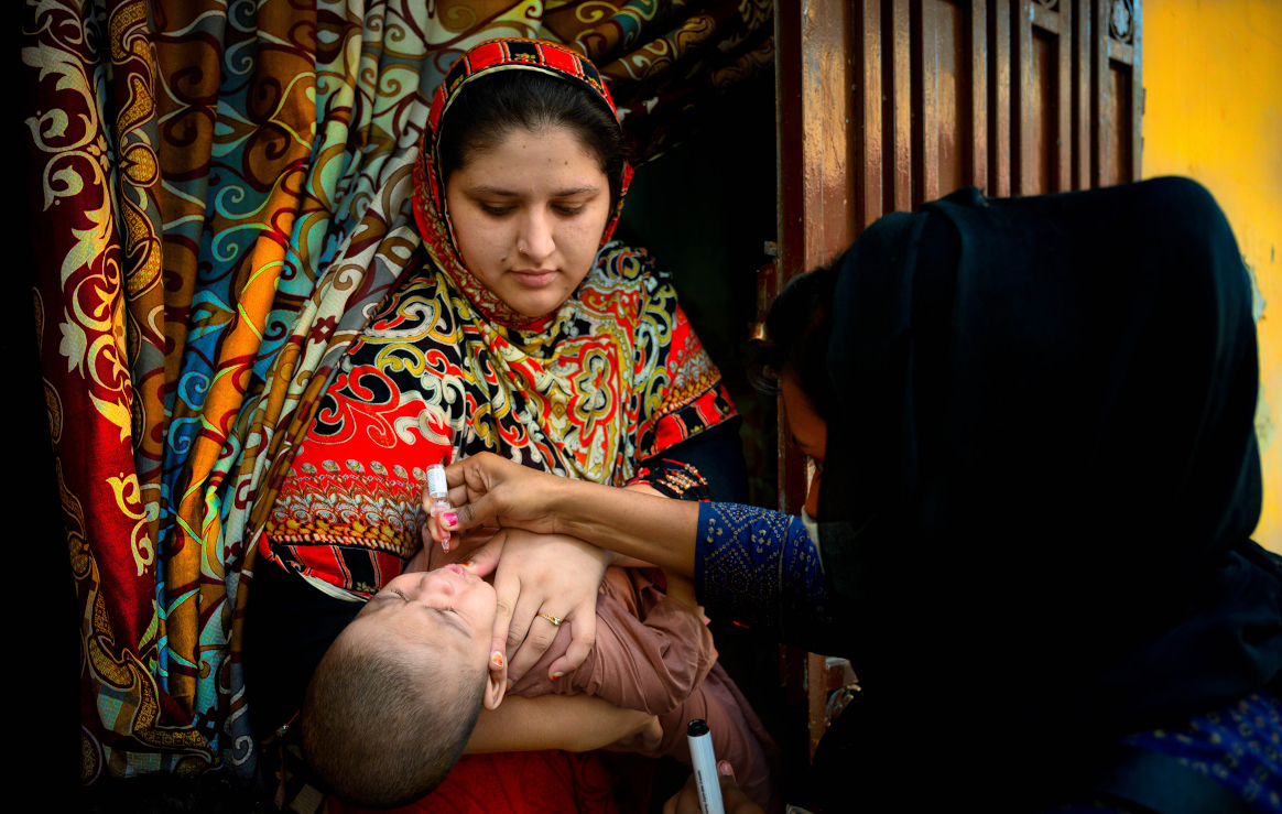 A polio worker, Shazia Bibi (right) vaccinates a seven month old boy held by his mother in a neighborhood in Rawalpindi, Pakistan. © UNICEF/Pakistan/Bokhari.