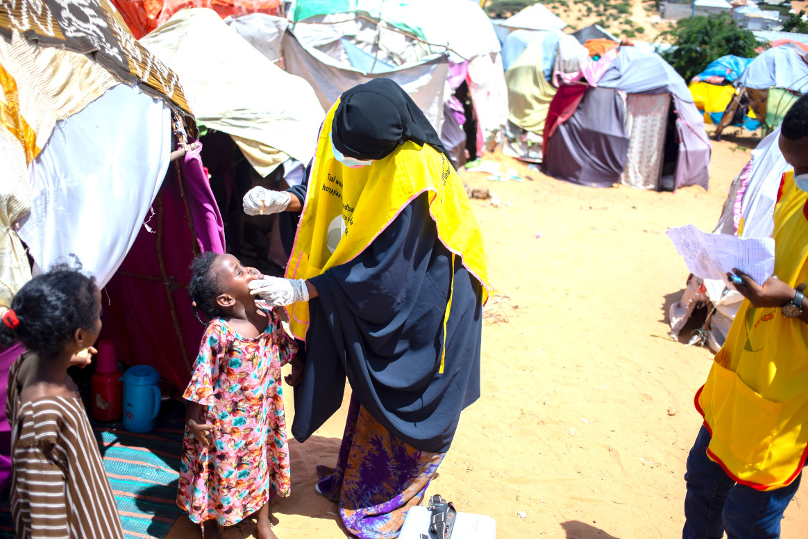 A health worker administers polio vaccine (nOPV2) drops to a child at Luley IDP camp during a door-to-door polio  immunization campaign in Kahda district, Mogadishu, Somalia on May 28, 2023. © Ismail Taxta/Getty Images